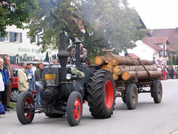 Ein Oldtimer-Traktor zieht einen mit Holzstämmen beladenen Anhänger entlang der Schwabenstraße 
