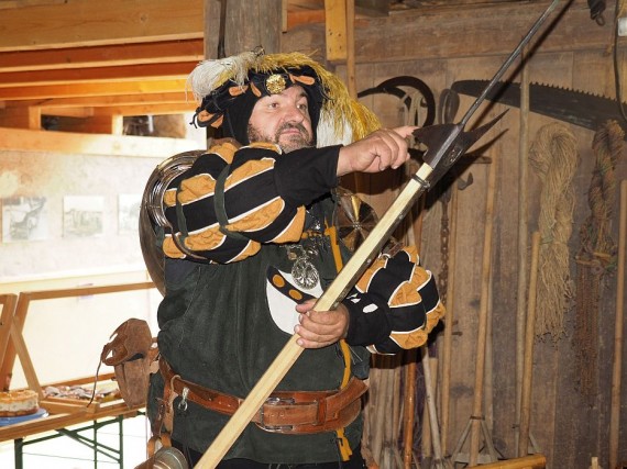 Ein Ritter in schwarz-gelber Kleidung prüft seine Hellebarde in der Tenne des Baschtlehauses