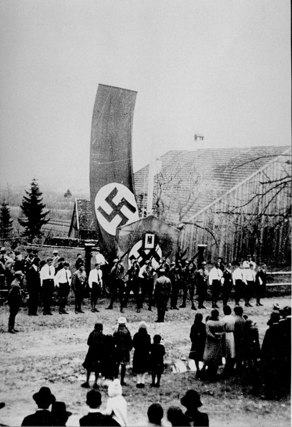 Salutschützen vor einer großen Hakenkreuz-Fahne auf dem Dorfplatz 1933